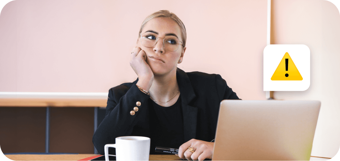 Professional wearing glasses and black blazer sits at desk with coffee cup, looking contemplative against pink background